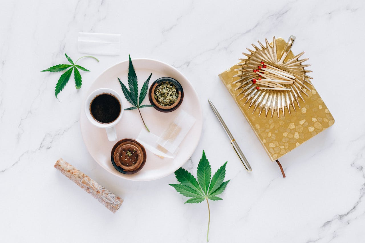 about-02 Top view of cannabis leaves, coffee, grinder, and matches on a marble surface, creating a relaxed setting.