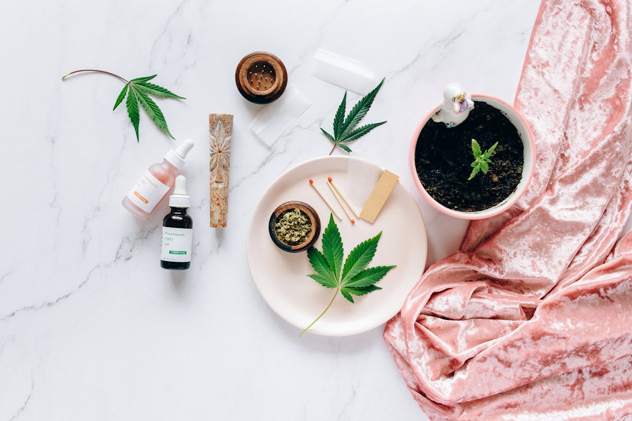 about-03 Flat lay of cannabis leaves, CBD oils, and accessories on marble surface.
